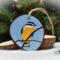 A hand-painted red-breasted nuthatch with sky blue background on a wood slice ornament at Cove Creek Photography.